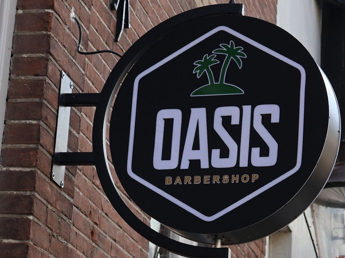Het ronde uithangbord van Oasis barbershop aan de bakstenen gevel