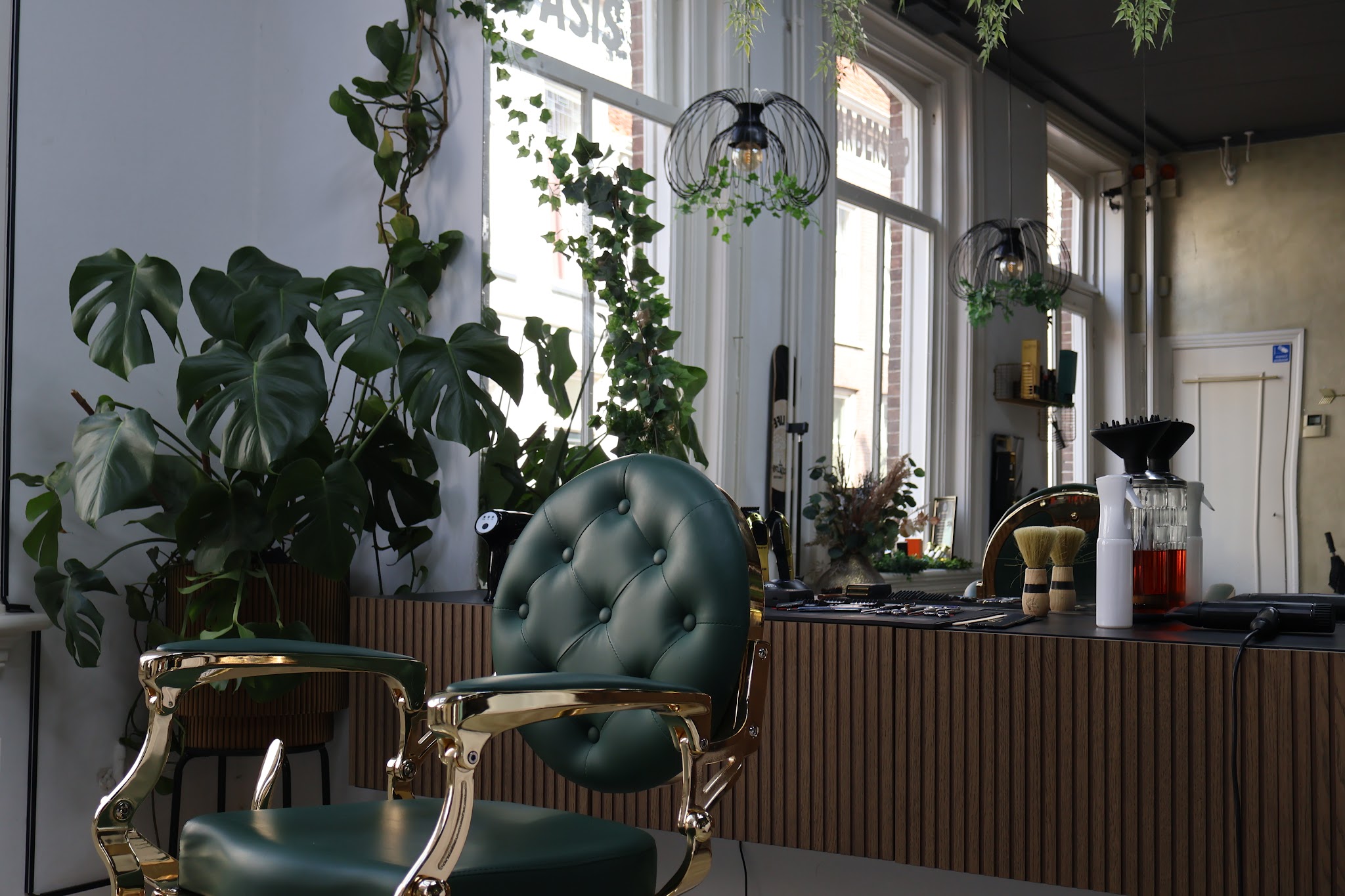 Groene barberstoelen met gouden frame tussen de planten, bij de hoge ramen
