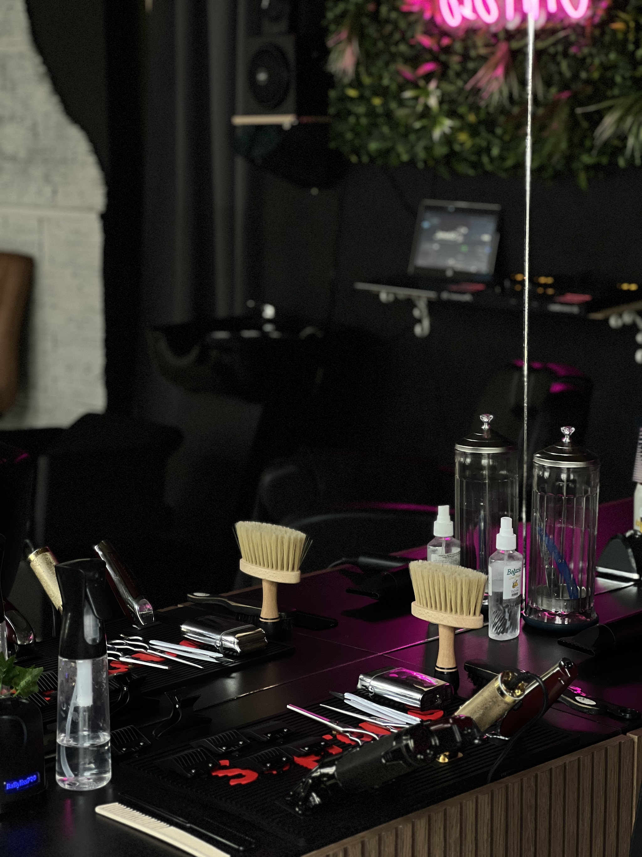 Werkplek van Oasis barbershop met kwasten, tondeuses en roze neon voor de plantenwand