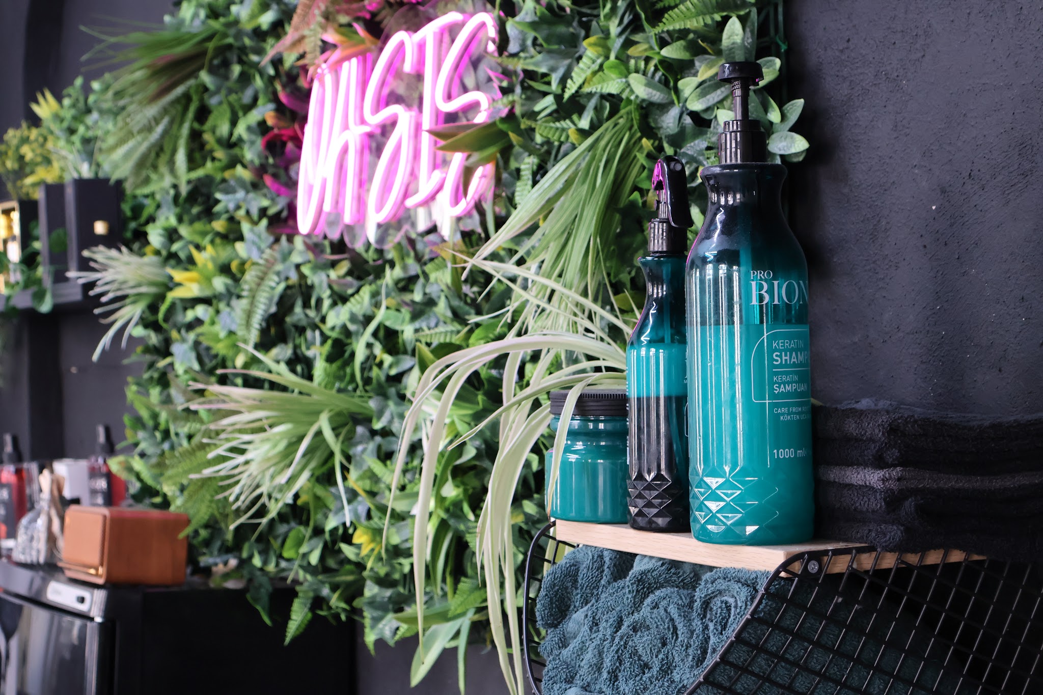 Roze neon OASIS op een groene plantenwand, met flessen shampoo ervoor